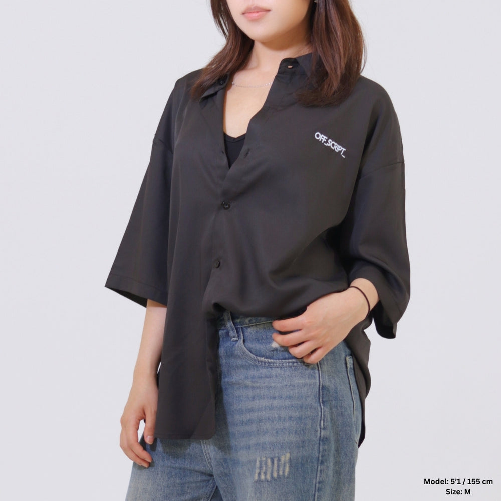 Person wearing a black oversized shirt with a brand logo on a plain background