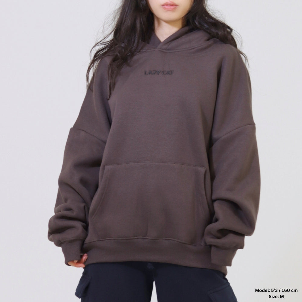 Person wearing a brown hoodie with 'LAZYCAT' logo on a plain background