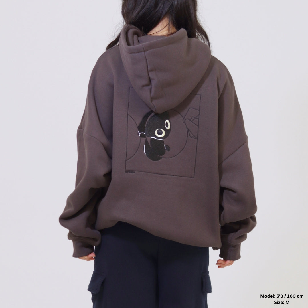 Person wearing a brown hoodie with a black and white design on the back against a plain background