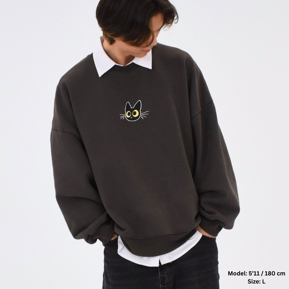 A person wearing a dark green fully embroidered sweater with a graphic design on the back, over a white shirt.