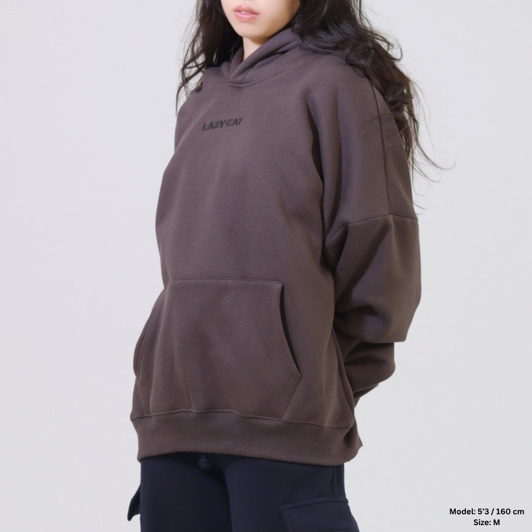 Person wearing a brown hoodie with a brand logo on a plain background