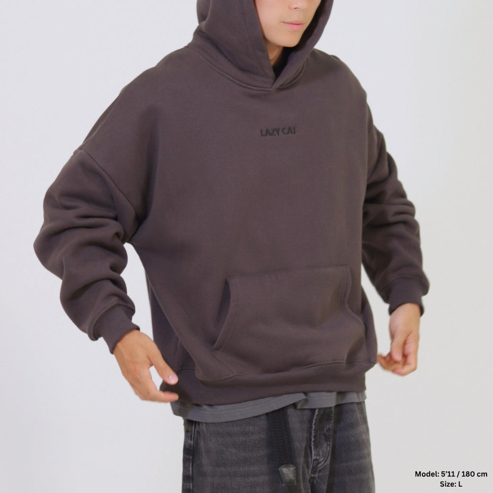 Person wearing a brown hoodie with a visible brand logo on a plain background