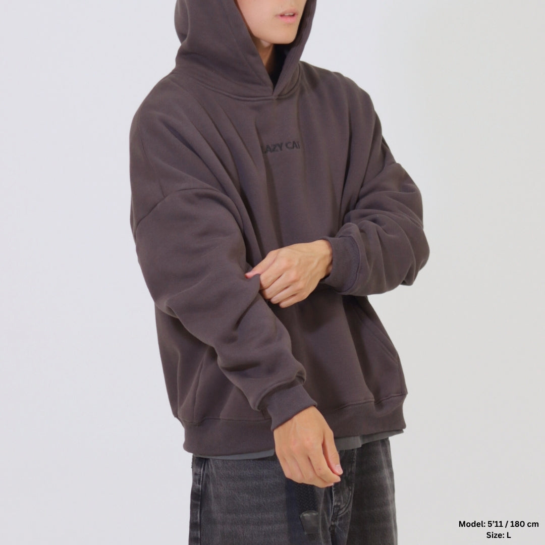 Person wearing a dark brown hoodie with a brand logo on a light gray background