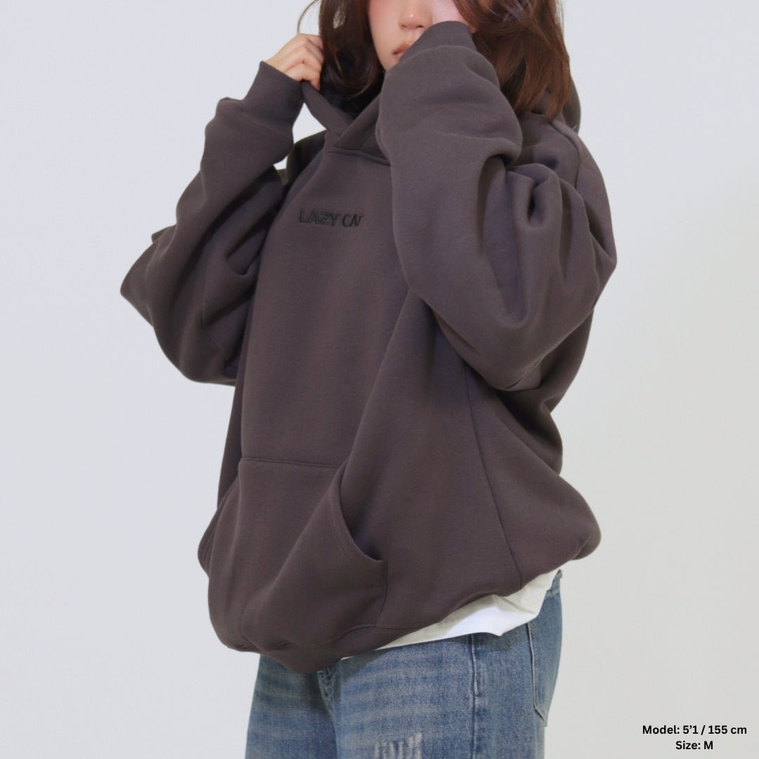 Person wearing a dark brown hoodie with 'LAZY OAF' branding on a white background