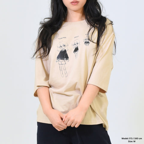 Person wearing a beige oversized t-shirt with graphic design on a plain background