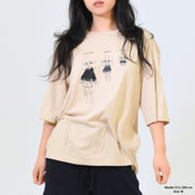 Woman wearing a beige oversized shirt with graphic designs on a plain background