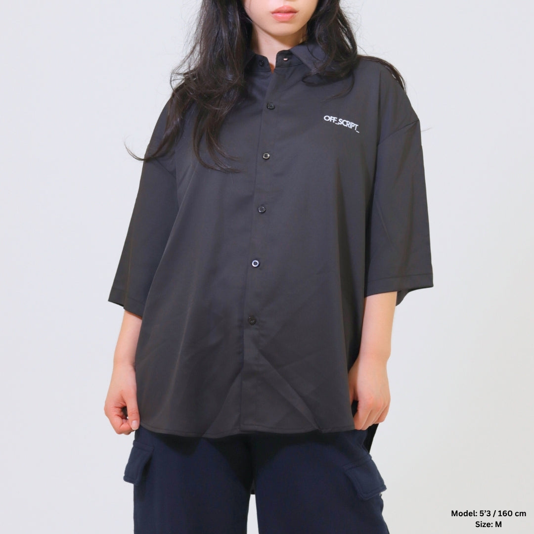 Person wearing a black oversized shirt with a brand logo on a plain background