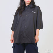 Person wearing a black oversized shirt with a brand logo on a plain background