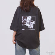 Person wearing a black oversized shirt with a graphic design on the back against a plain background