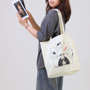 Person holding a tote bag with a design and a phone, against a plain background