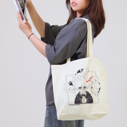 Person holding a tote bag with cartoon designs on a plain background
