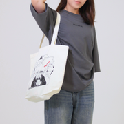 Person holding a white tote bag with black graphics against a plain background