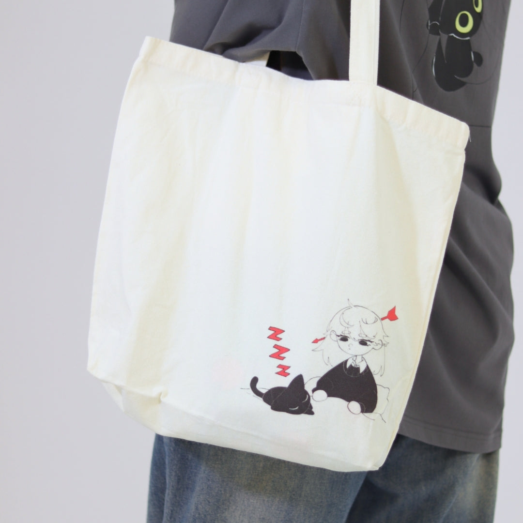 Person holding a tote bag with a design of a cat and a person, against a plain background