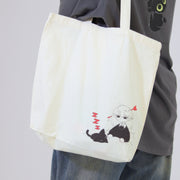 Person holding a tote bag with a design of a cat and a person, against a plain background