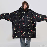 Person wearing a large black hoodie with cat face patterns on a white background
