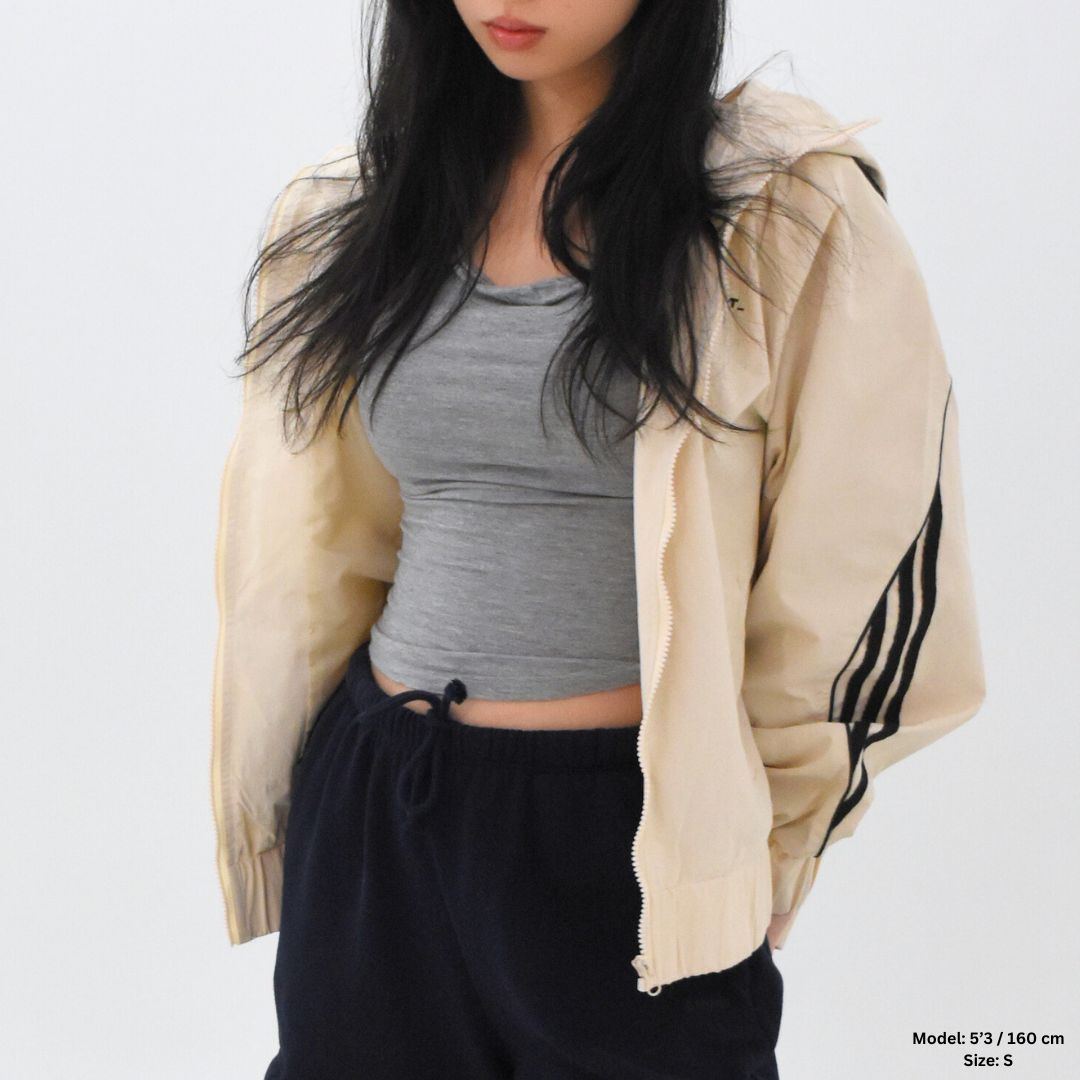 Person wearing a beige Adidas jacket over a gray top and black pants on a white background