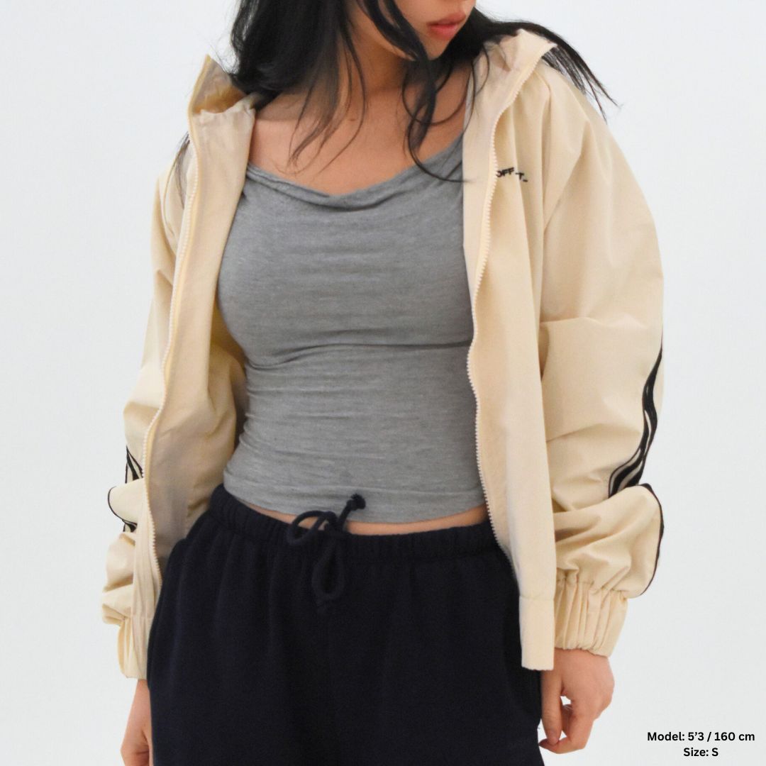 Person wearing a beige jacket, gray top, and black pants on a white background