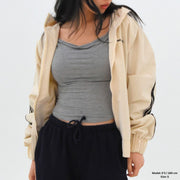 Person wearing a beige jacket, gray top, and black pants on a white background